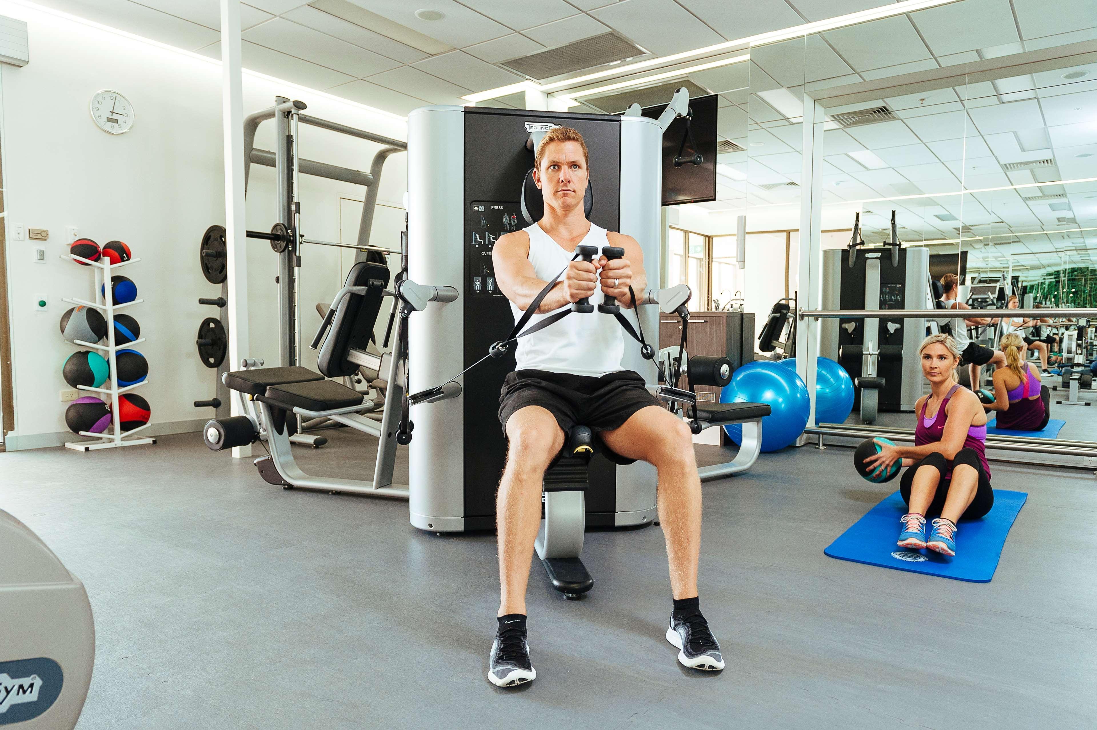 Stamford Plaza Adelaide Hotel Kültér fotó The photo shows a gym setting with two individuals engaged in workout activities. 

In the foreground, a man is seated on a machine, using the handles to perform a rowing exercise. He is wearing a sleeveless shirt and shorts, indicating an active wor