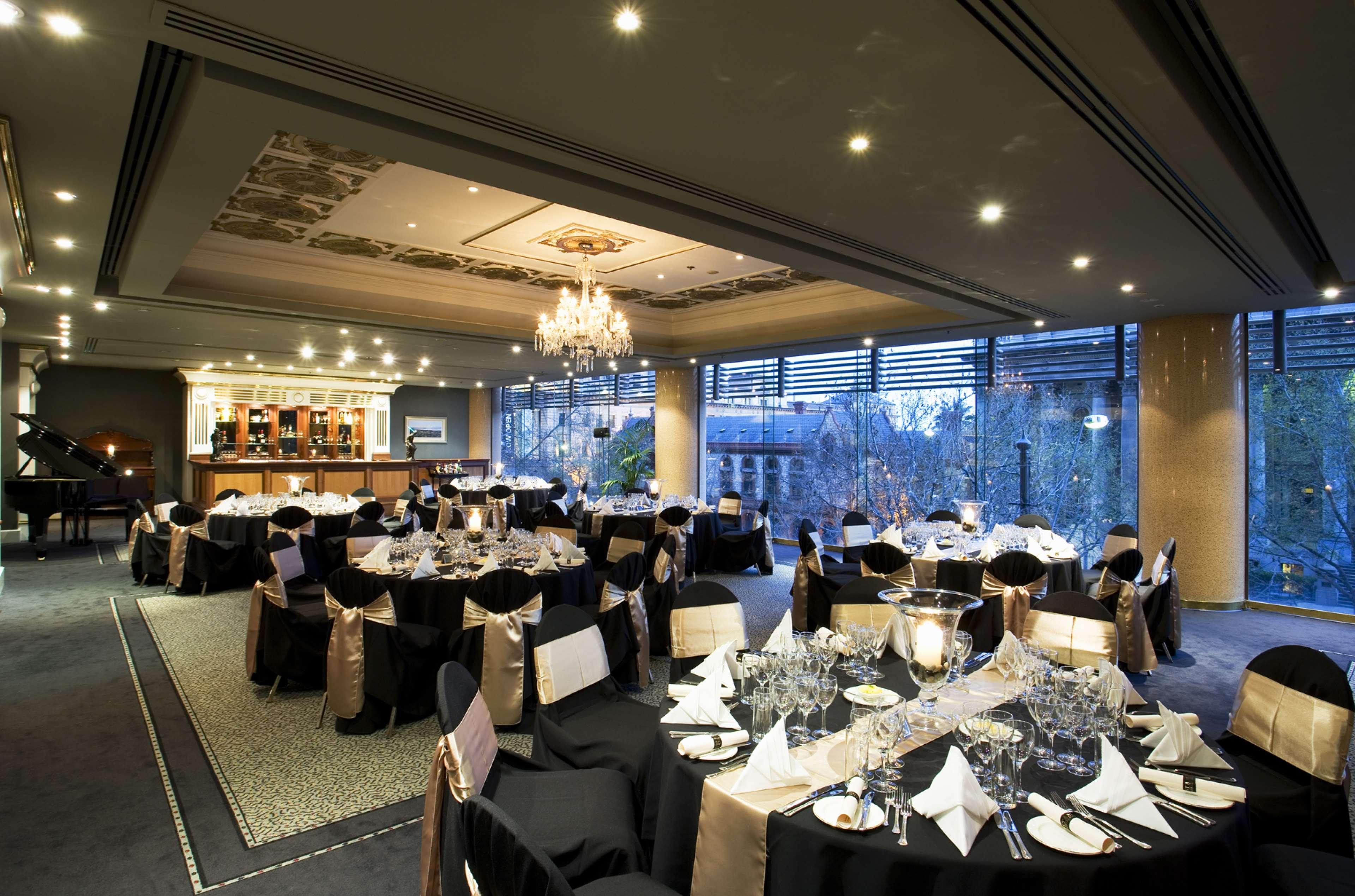 Stamford Plaza Adelaide Hotel Kültér fotó The photo shows an elegant banquet hall or restaurant setting. There are several round tables covered with black tablecloths and adorned with gold accents. Each table is set with fine dining utensils, glassware, and neatly folded napkins. In the back