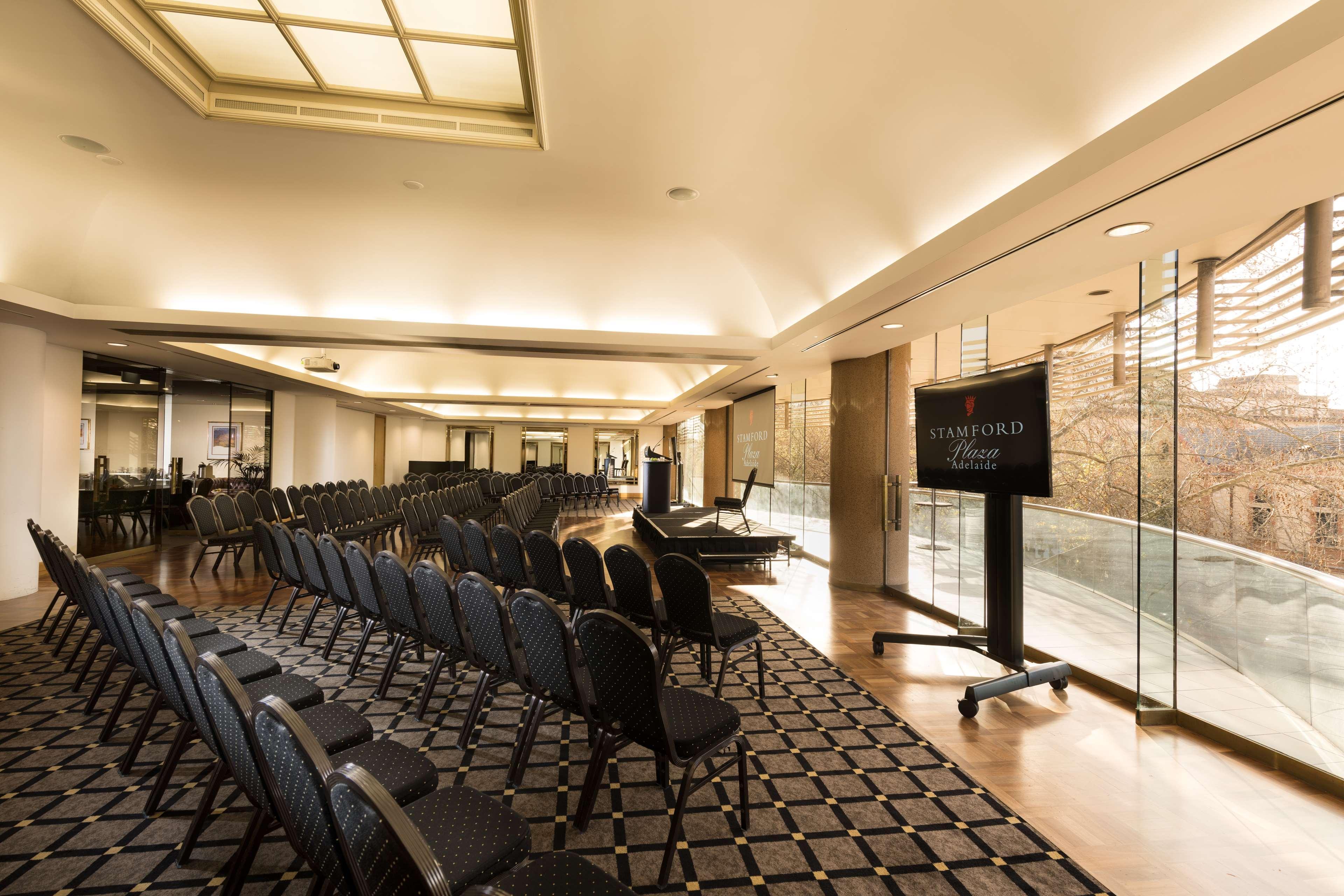 Stamford Plaza Adelaide Hotel Kültér fotó The photo shows a large, elegantly designed event space or meeting room. There are rows of black chairs set up facing a presentation area. The flooring features a patterned carpet, and large windows allow natural light to enter the room. On one side,