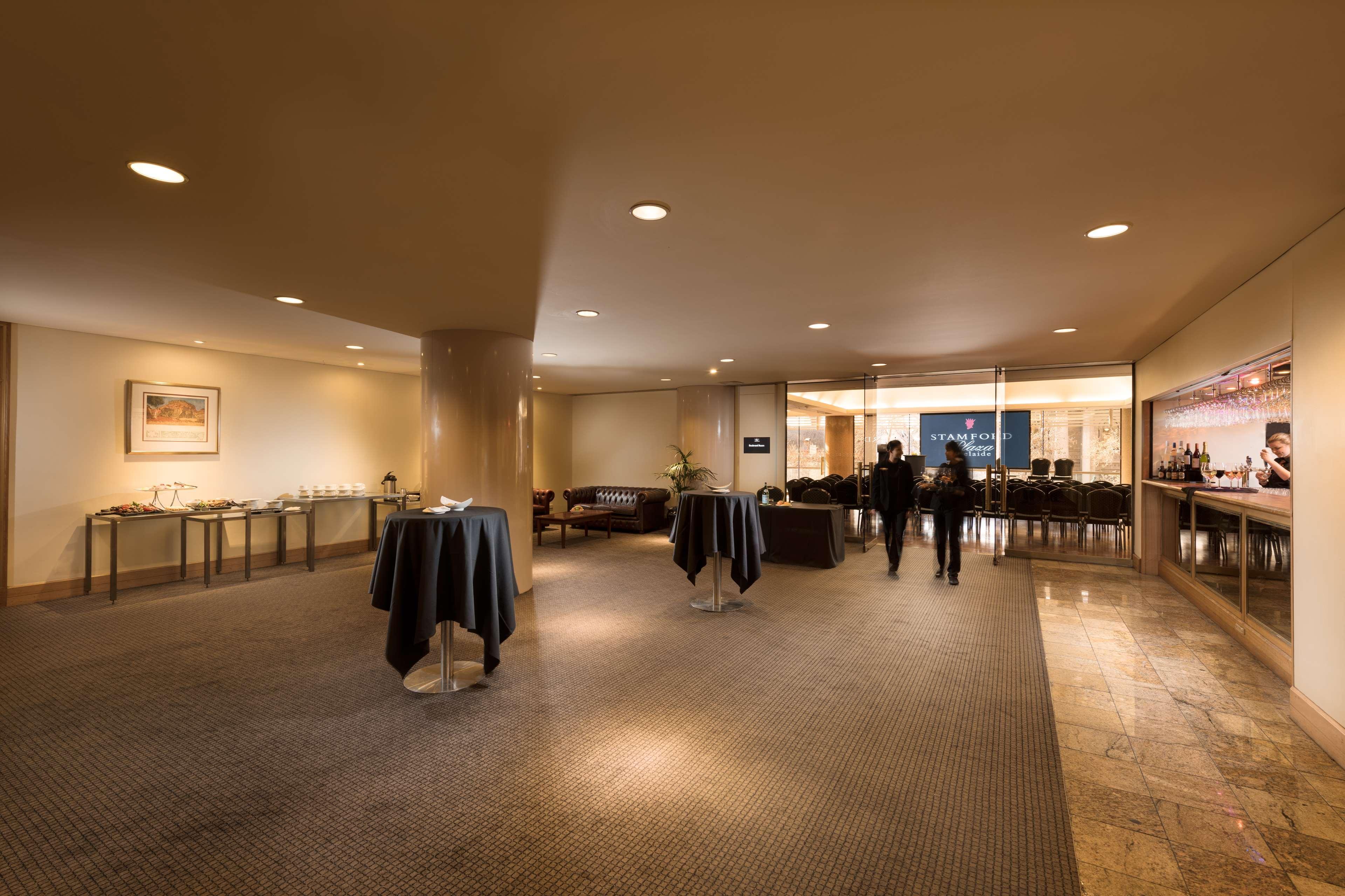 Stamford Plaza Adelaide Hotel Kültér fotó The image shows an indoor space that appears to be a lounge or reception area. There are several round tables with dark tablecloths positioned throughout the room. The floor is carpeted, and the lighting is warm and somewhat dim. In the background, t