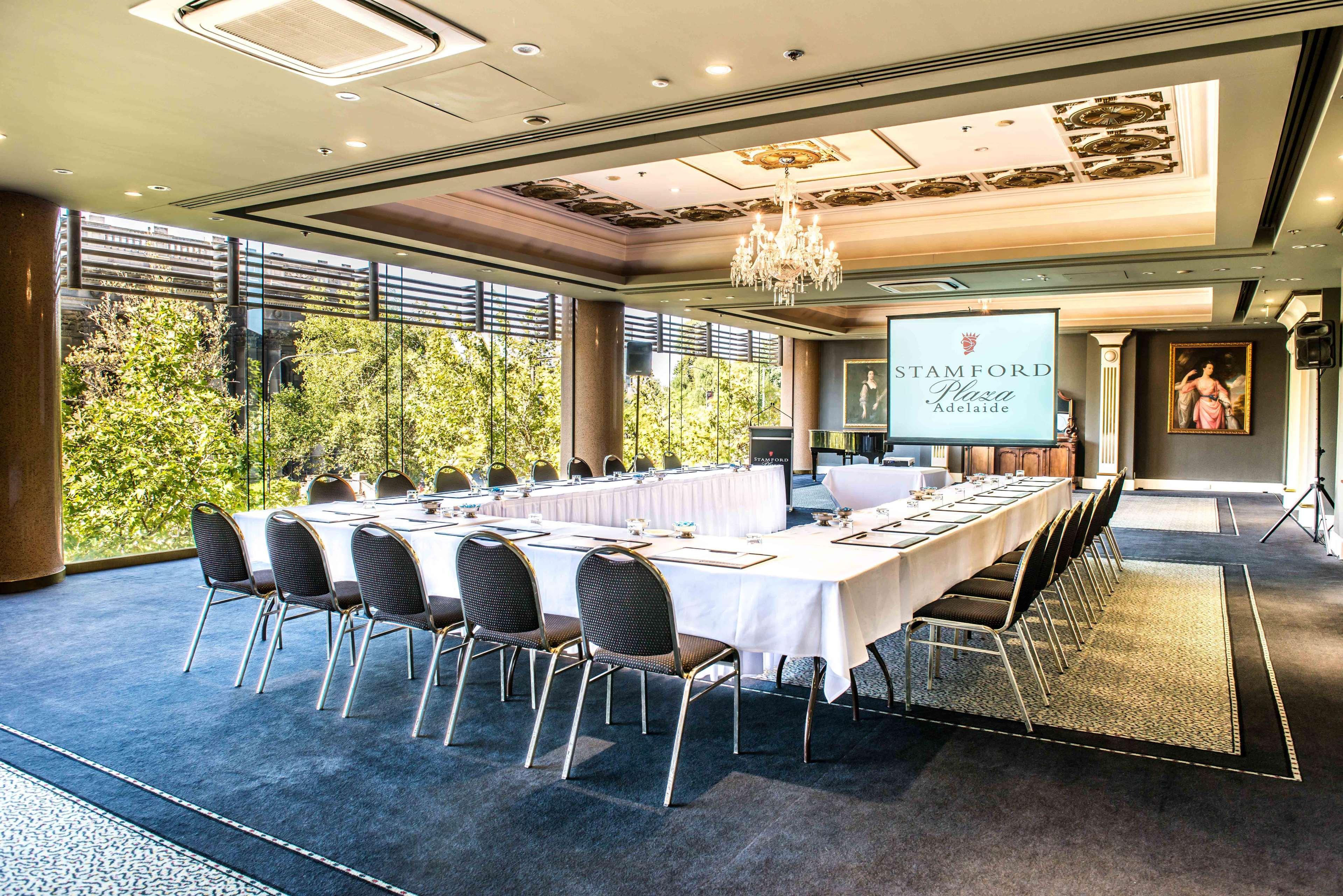 Stamford Plaza Adelaide Hotel Kültér fotó The photo shows a stylish conference room set up for a meeting or event. There is a long rectangular table covered with a white tablecloth, surrounded by black chairs. A large screen displays the name "Stamford" along with a logo. The room features l