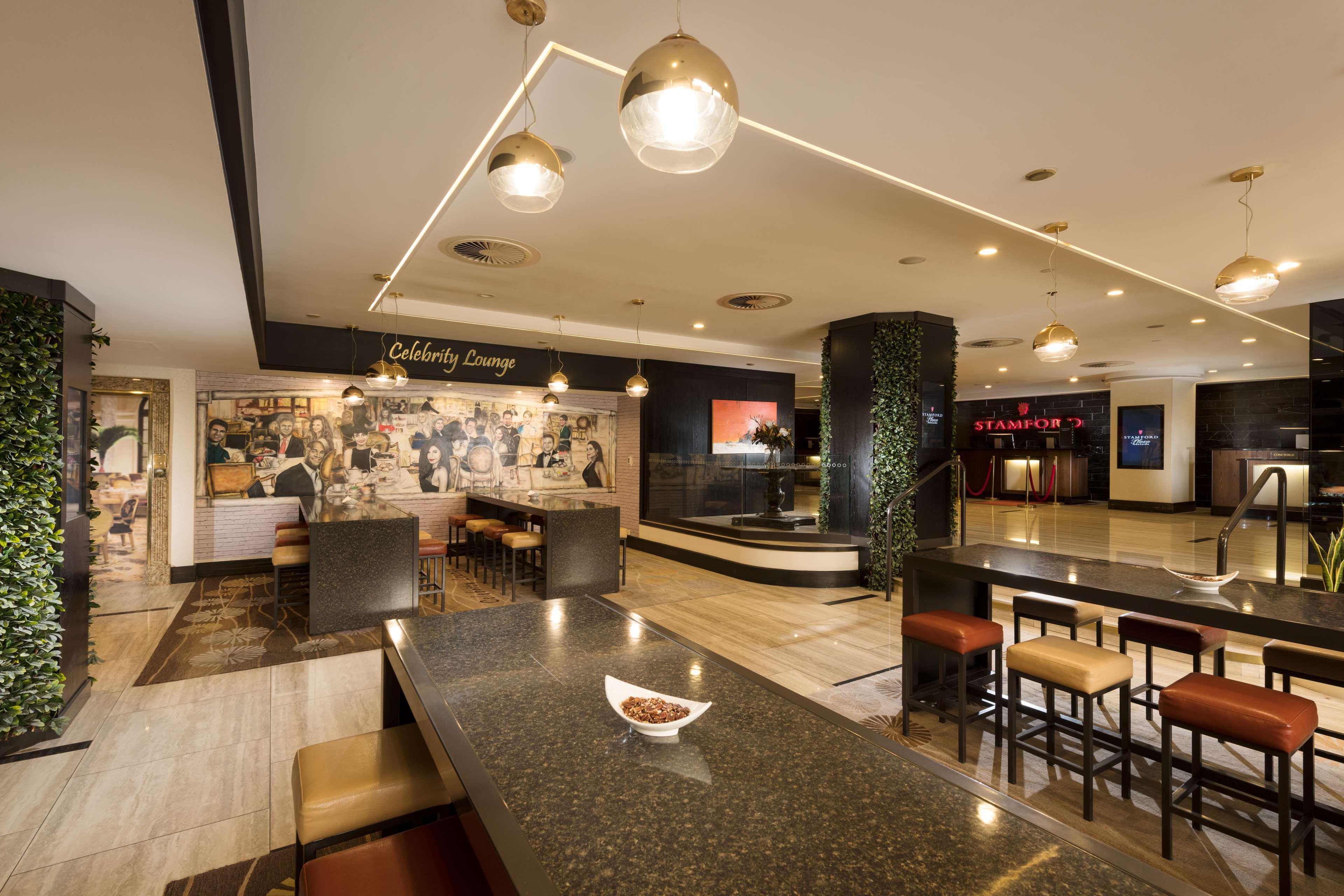 Stamford Plaza Adelaide Hotel Kültér fotó The photo shows a modern and stylish interior of a lounge or restaurant area. Prominent features include a long dark countertop with bar stools, and several pendant lights hanging from the ceiling. In the background, there is a mural or artwork that 