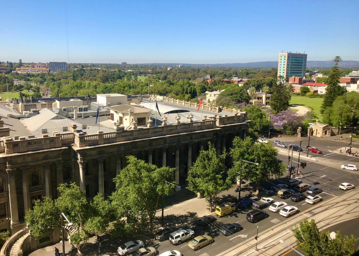 Stamford Plaza Adelaide Hotel Kültér fotó The photo depicts a cityscape view, showcasing a mix of architectural structures and greenery. In the foreground, there is a large, classical building with columns, suggesting it may be a historical or governmental structure. Surrounding the building